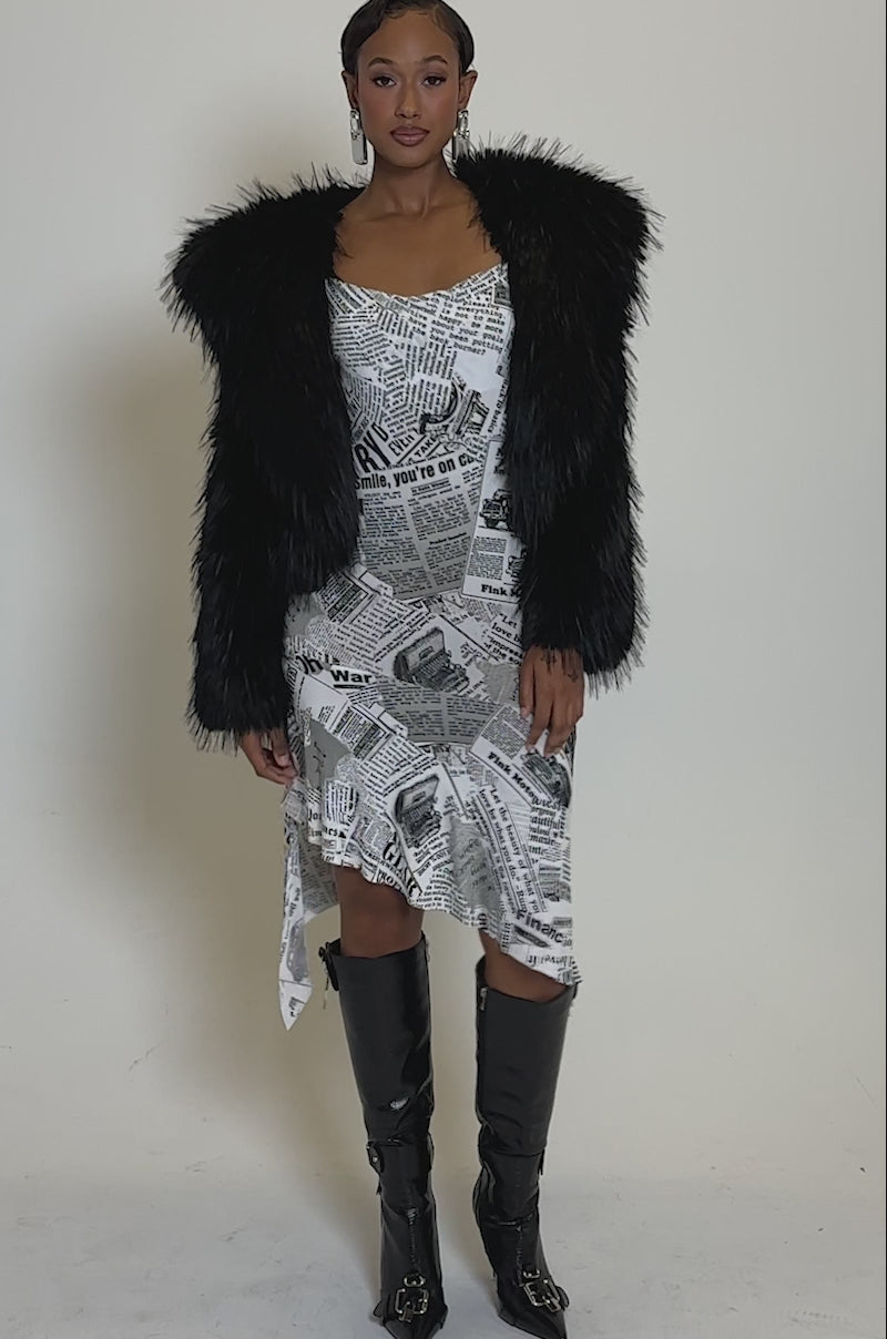 Video of woman modeling the LOSING IT HOODED FAUX FUR jacket over a newspaper-print fitted dress, accessorized with bold rectangular earrings, set against a plain light background.