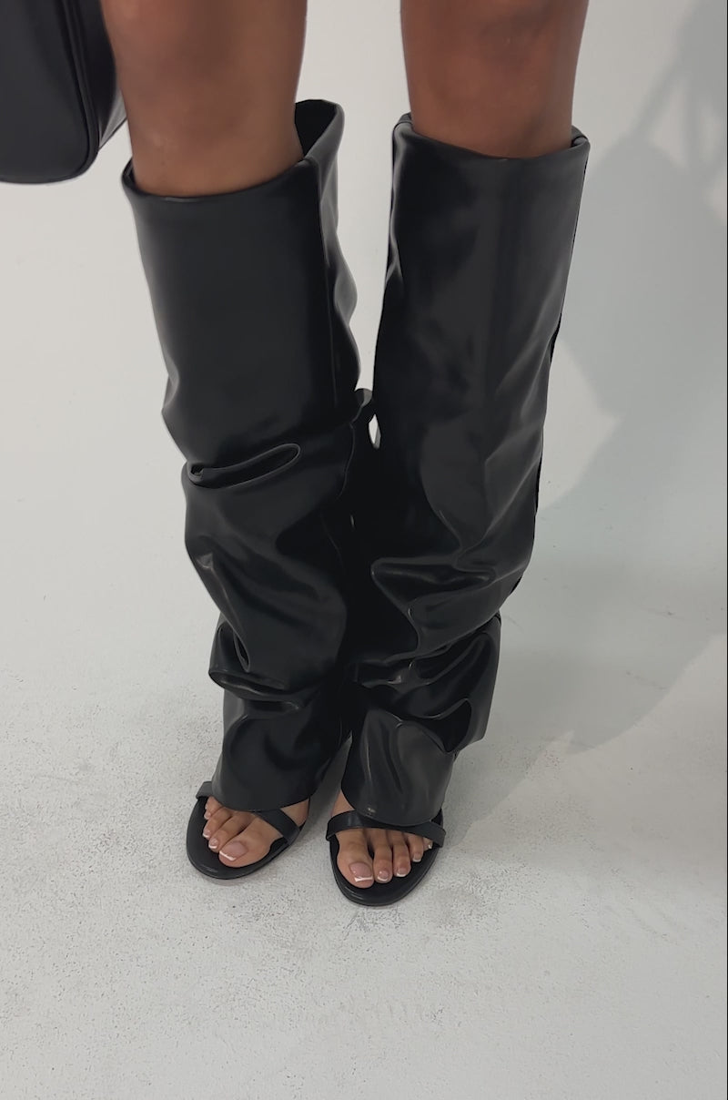 Video of woman modeling the AZALEA WANG RAYLAN BLACK GLADIATOR SANDAL with open toes and high heels, paired with a structured black handbag, creating a bold, modern look reminiscent of stylish knee-high gladiator sandals.