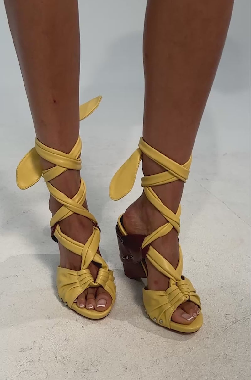 Video of woman modeling the AZALEA WANG ARUBA YELLOW BLOCK HEEL TIE UP SANDAL—strappy yellow faux leather sandals with ankle ties and brown block heels