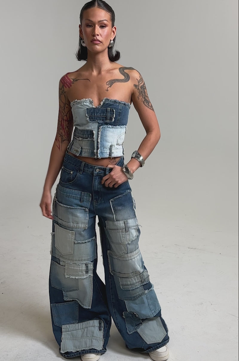 A video of a person in the PATCH ME UP DENIM CORSET and wide-leg pants with large patch pockets, slicked-back hair, hoop earrings, and a bold metallic bracelet.