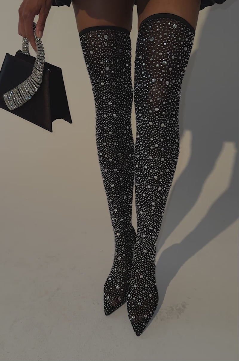 Video of a woman modeling the AKIRA GOLD PIA BLACK RHINESTONE MESH THIGH HIGH BOOT, featuring sparkling rhinestones, a pointed toe, and a stiletto heel.