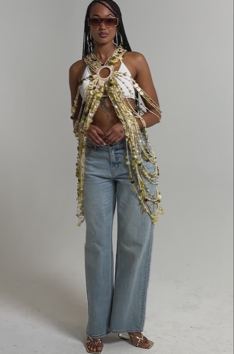 A video of a woman wearing the SHAKE IT GIRL CROCHET TOP with gold chains and discs, paired with light blue wide-leg jeans, gold heeled sandals, sunglasses,  and layered jewelry.