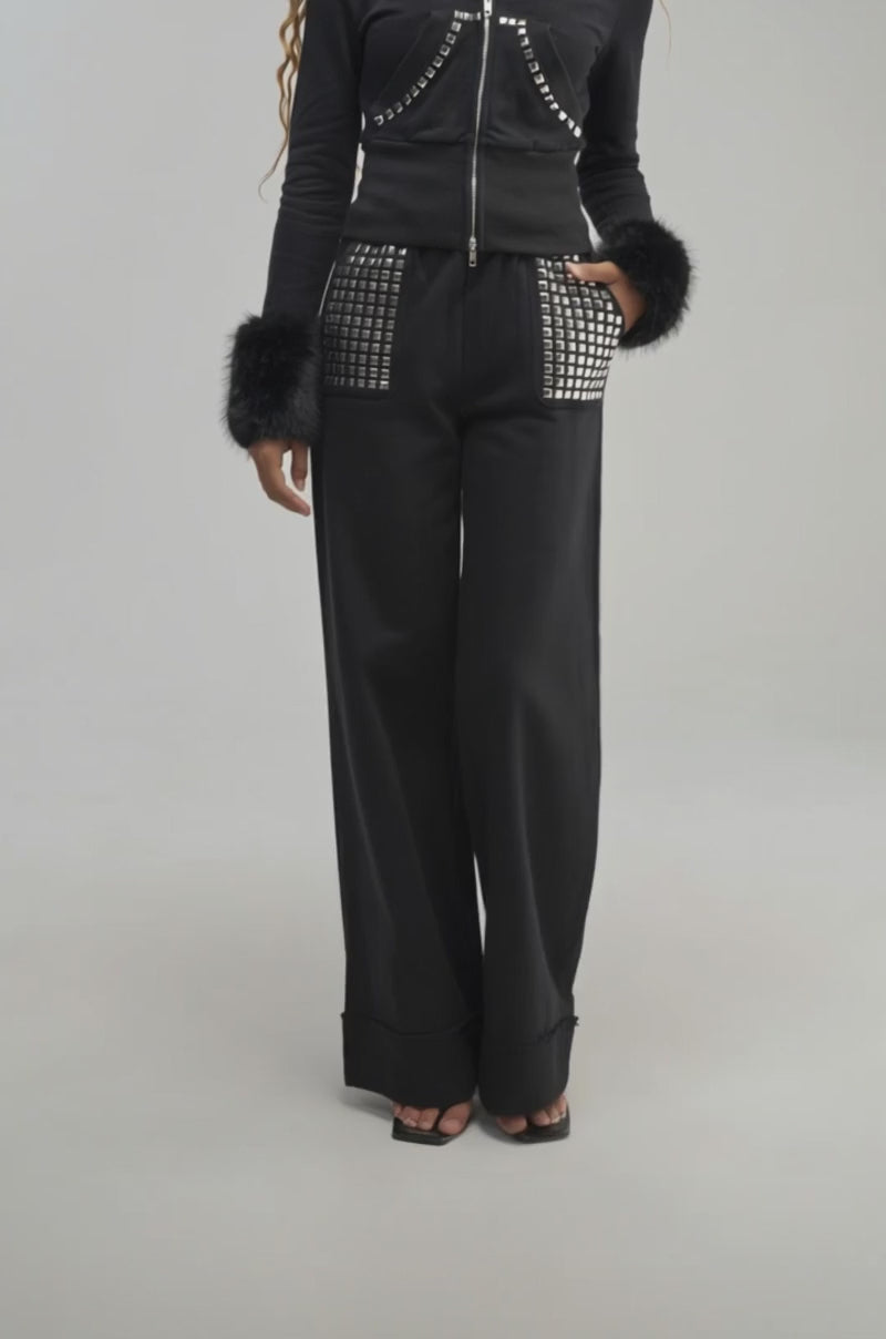 Video of a woman modeling the BLESSED WIDE LEG JOGGER—black jogger pants featuring large silver-studded pockets.