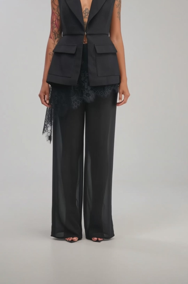 Video of a woman modeling the NAOMI BLAZER VEST IN BLACK and lace pants, holding a black bag, standing against a plain light background.