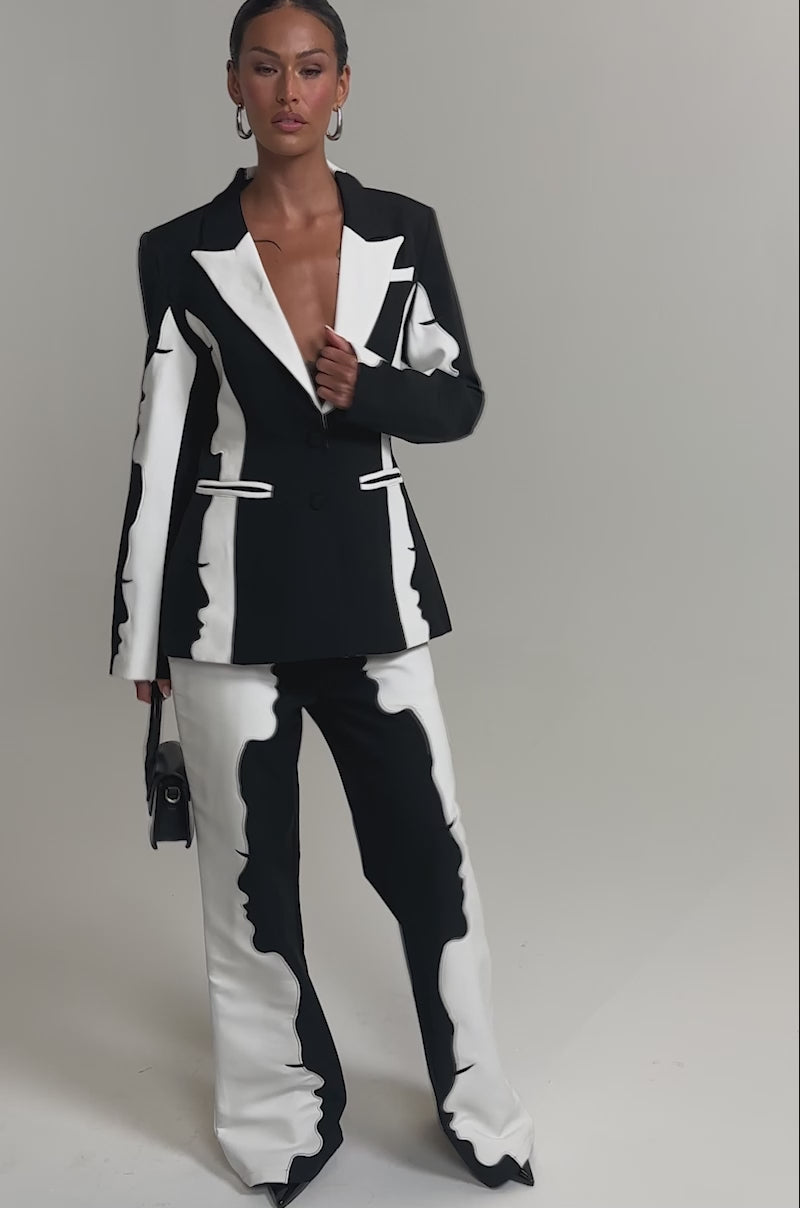 Video of woman modeling the POV GRAPHIC TROUSER—a high-rise, black and white wide-leg suit trouser with an abstract pattern—paired with a matching blazer and small black handbag against a plain light background.