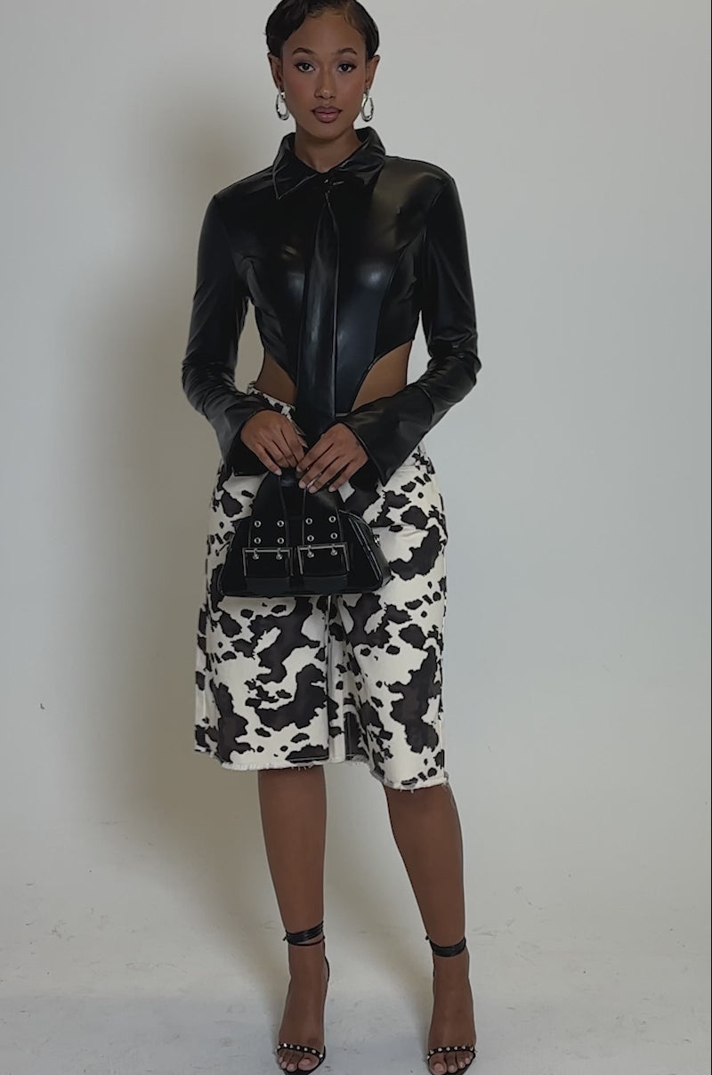 Video of woman modeling the ALWAYS EXTRA BUTTON DOWN BODYSUIT with cow-print pants and a black handbag. She accessorizes with hoop earrings 