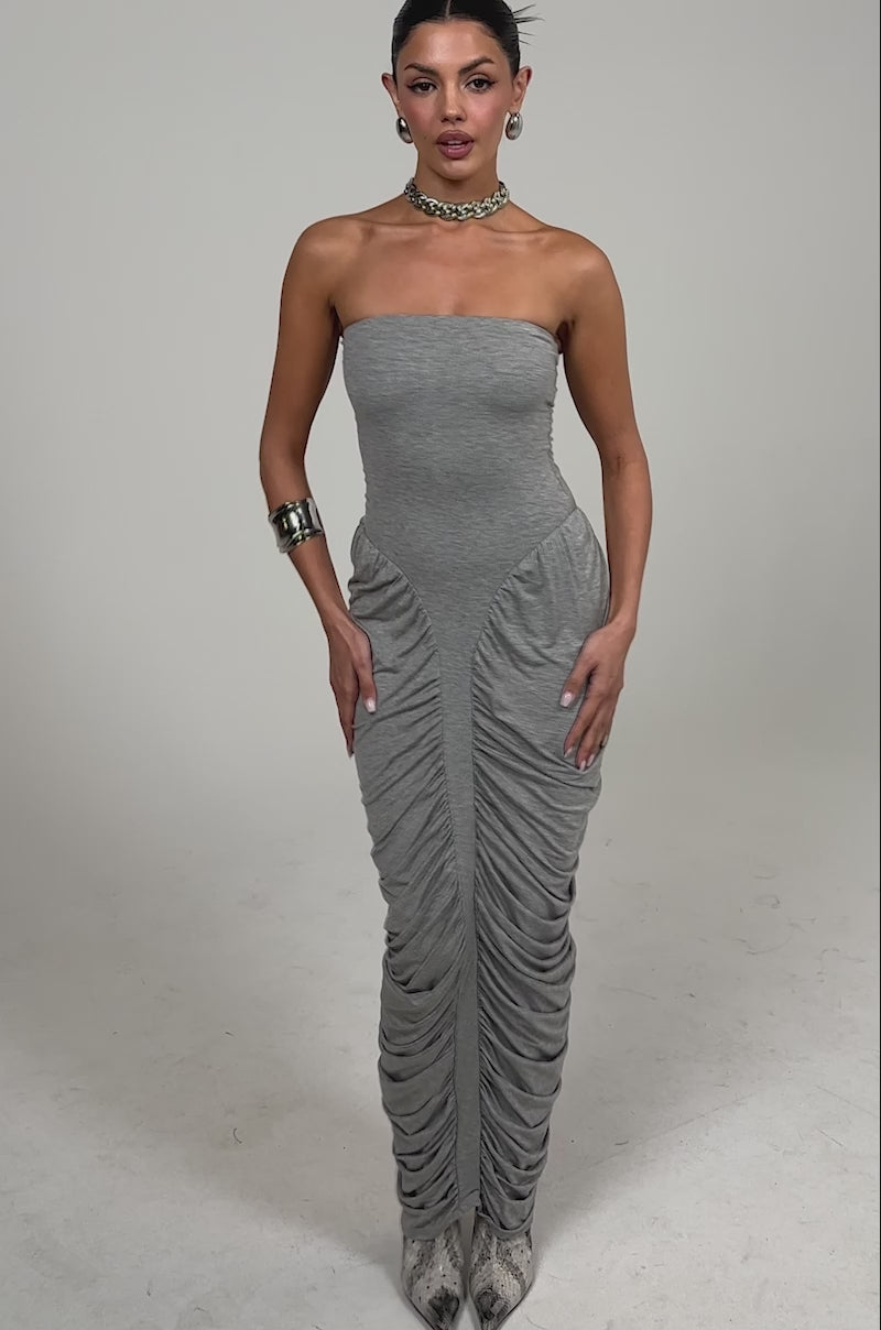 Video of woman modeling the CLASSIC CHIC STRAPLESS MAXI DRESS, a heather gray, ruched bodycon style. She pairs it with silver boots and bold jewelry, standing against a simple light background.