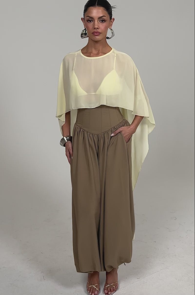 Video of woman modeling the FEELING LUXE CORSETED BALLOON PANT in tan, featuring a high-rise waistband and corset-like details, styled with a flowy yellow top, metallic bracelet, and strappy heeled sandals. 