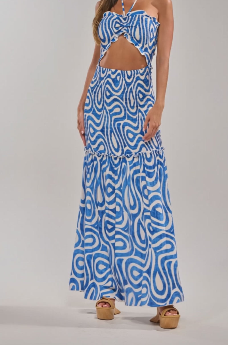 Video of woman modeling the SUGAR AND SPICE PRINTED MAXI DRESS IN BLUE MULTI, a sleeveless abstract print dress with a halter neck and front cutout, standing against a plain light background.