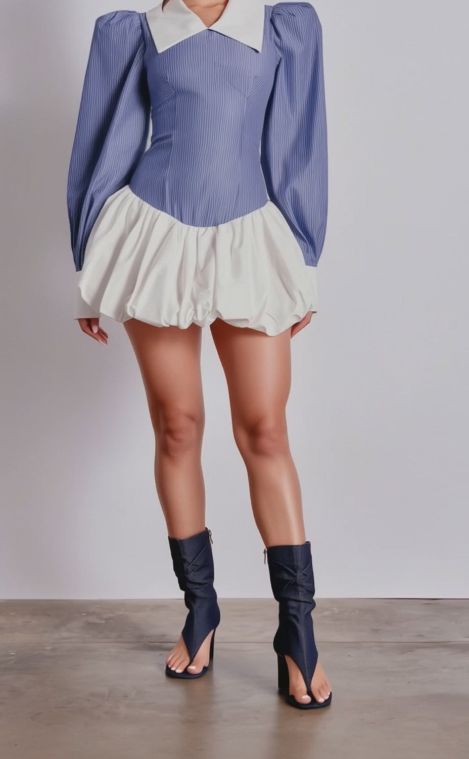 A video of a woman in the CHELSEA LONG SLEEVE STRIPE MINI DRESS, featuring blue pinstripes, a fitted bodice, white collar, and puffy skirt. 