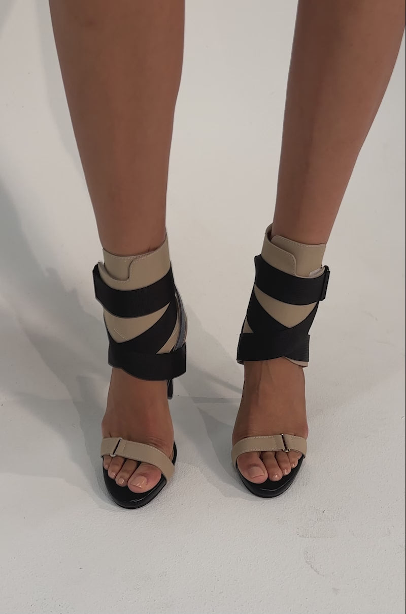 A video of a person in the AZALEA WANG KIVA KHAKI STILETTO SPORTY SANDAL with wide black crisscross elastic straps and a comfort cushion insole, standing on a light background. 