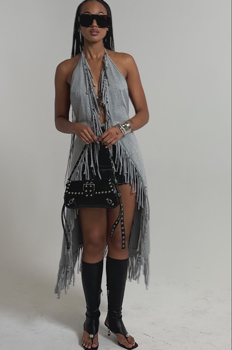 A video of a woman in the FRINGE GIRL BLOUSE—heather gray with boho fringe—paired with a black mini skirt, knee-high open-toe boots, sunglasses, and a belt-accented purse.
