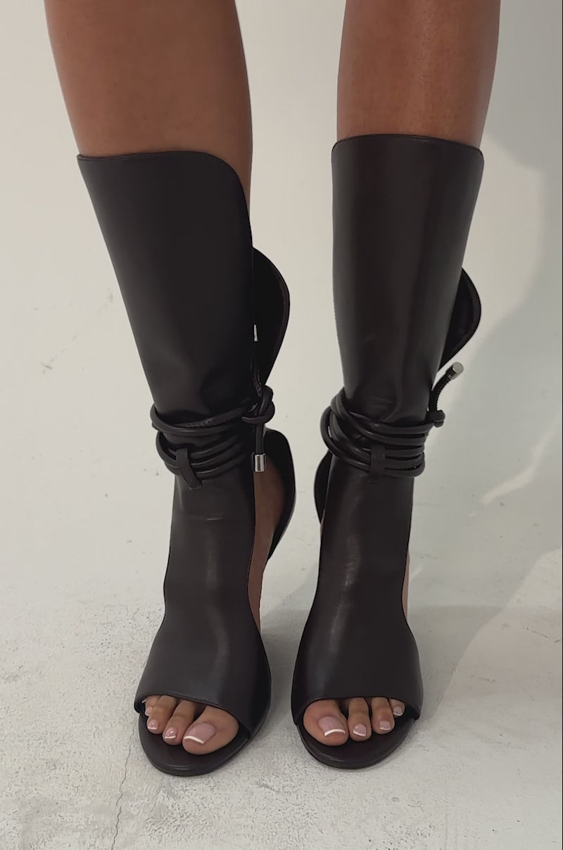 A video of a person wearing a tiered leopard print skirt and the AZALEA WANG DOUMA CHOCOLATE WEDGE LACE UP TALL SHAFT SANDAL.