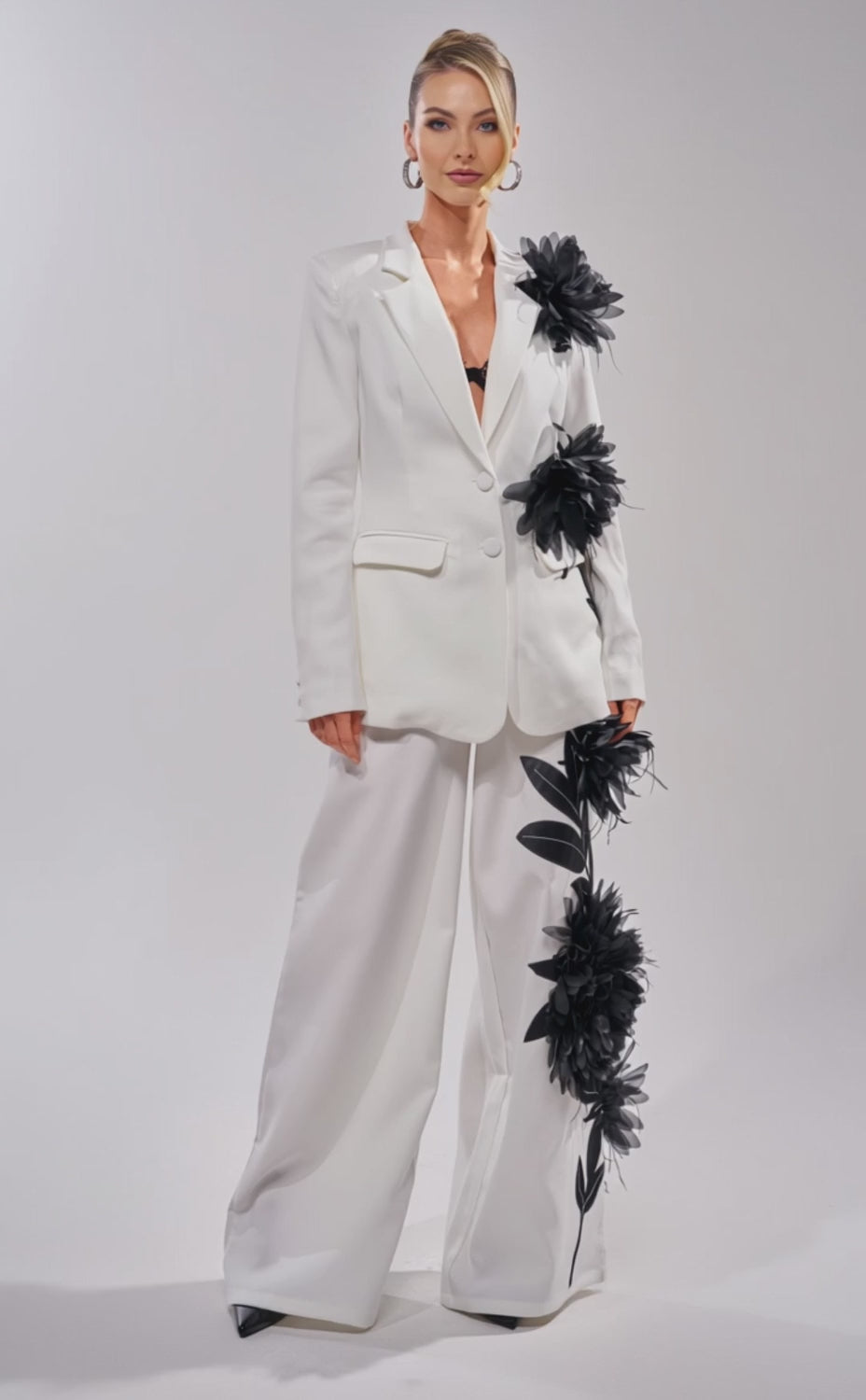 A video of a woman in the IN FULL BLOOM APPLIQUE BLAZER paired with wide-leg pants and a black lace top. 