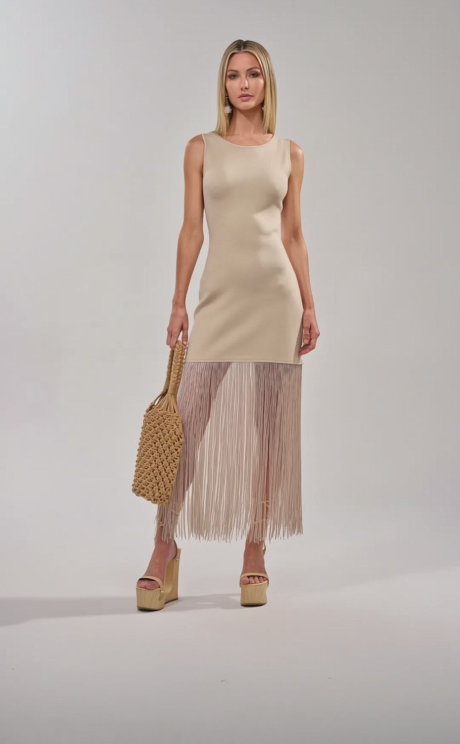 Video of woman modeling the FLY AWAY KNIT MIDI DRESS WITH FRINGE in beige, paired with a woven bag and neutral platform sandals, standing against a plain light background.