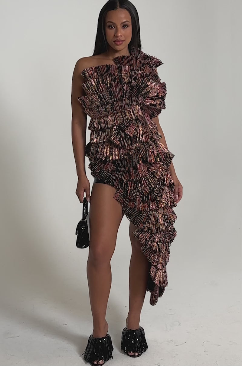A video of a woman in the RESTLESS NIGHTS ASYMMETRICAL BROCADE TOP with black shorts, fringed open-toe heels, and a small black handbag against a plain light background.