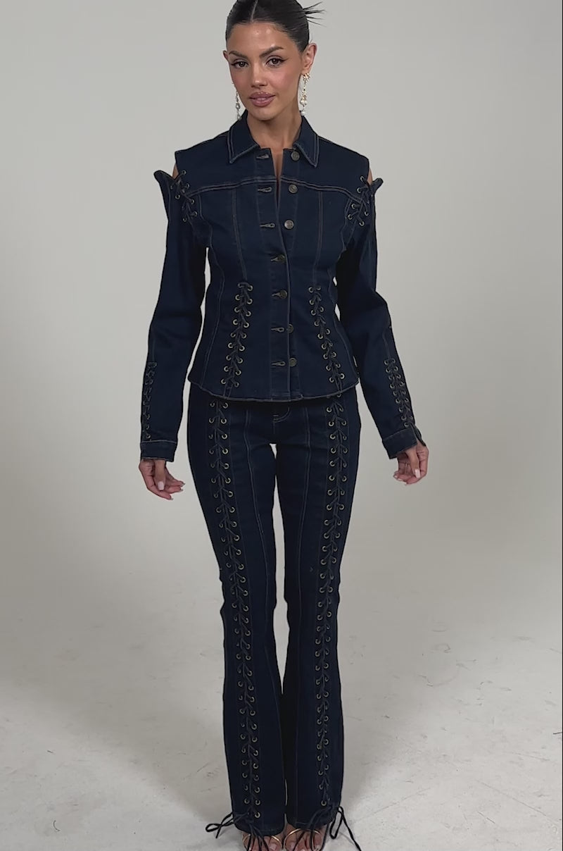Video of woman modeling the THATS ON ME FLARE DENIM PANT, styled with a matching dark denim jacket featuring lace-up details and cut-out shoulders against a plain light background.