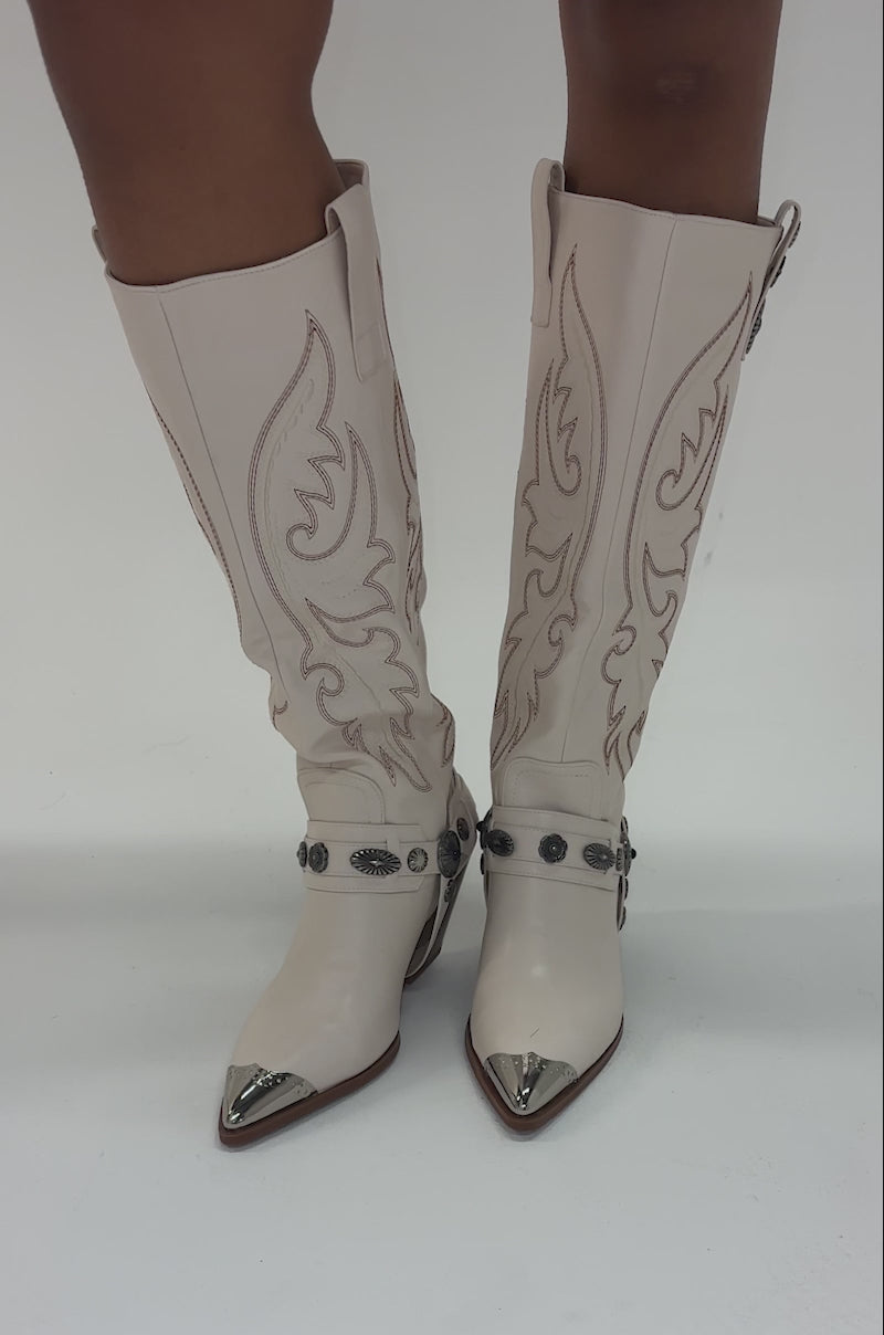 Video of woman modeling the AZALEA WANG GERVASE BONE PU SILVER HARDWARE WESTERN BOOT, featuring cream color, knee-high fit, decorative stitching, silver toe cap and metal accents