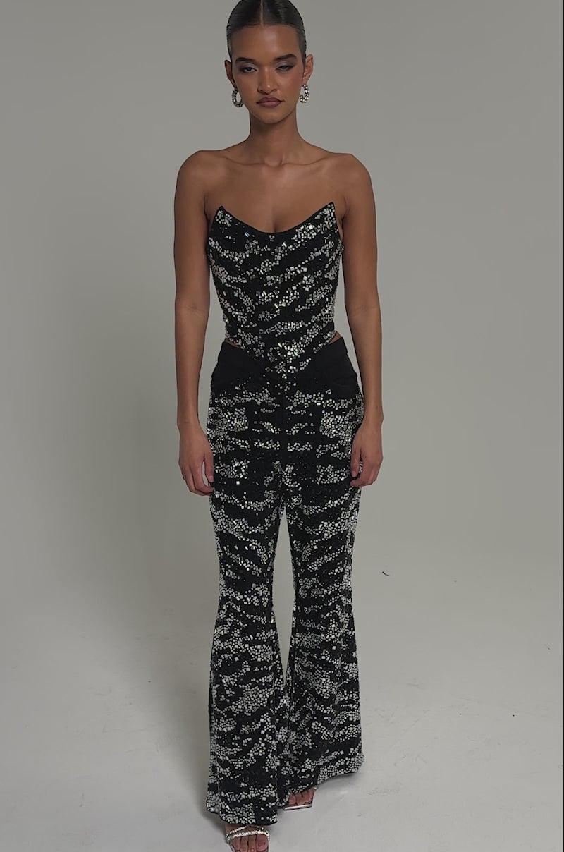 Video of woman modeling the TIME TO CELEBRATE AND DANCE RHINESTONE TROUSER—a high-rise, wide-leg pant featuring a shimmering abstract pattern—paired with a matching black sequined strapless top, set against a plain light background.