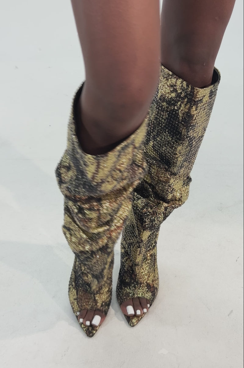 Video of woman modeling the AZALEA WANG YARDLEY MULTI GOLD RHINESTONE COVERED OPEN TOE BOOT—knee-high, pointed-toe boots with a shimmering gold and black pattern that add bold glamour to the look.