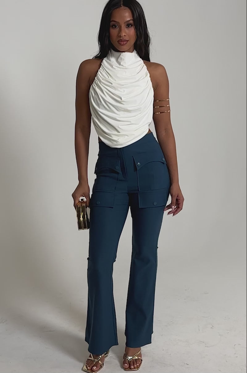 Video of woman modeling the TRY ME TROUSER blue high-rise flared utility pants with cargo pockets, gold heels, an arm cuff, and a small gold handbag.