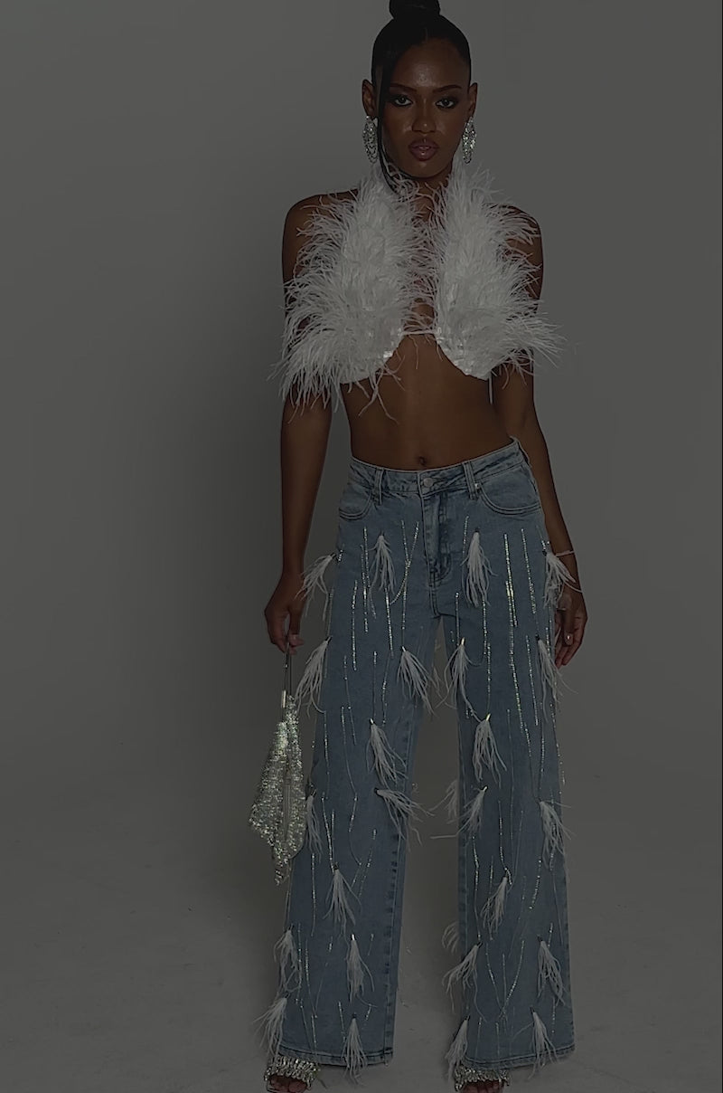 Video of woman modeling the SHAKE IT FOR ME GIRL FEATHER EMBELLISHED DENIM with a white feathered halter top, styled with a small bag and strappy heels.