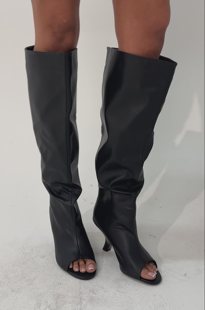 A video of a person wearing black leather shorts, a fuzzy black jacket, and the AZALEA WANG SIZANI BLACK WEDGE SLOUCHY BOOT.