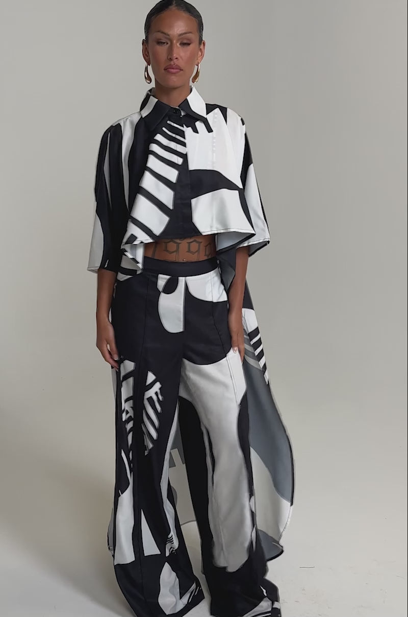A video of a woman in the NOIR GODDESS PALAZZO PANT paired with a flowing geometric top and large hoop earrings.