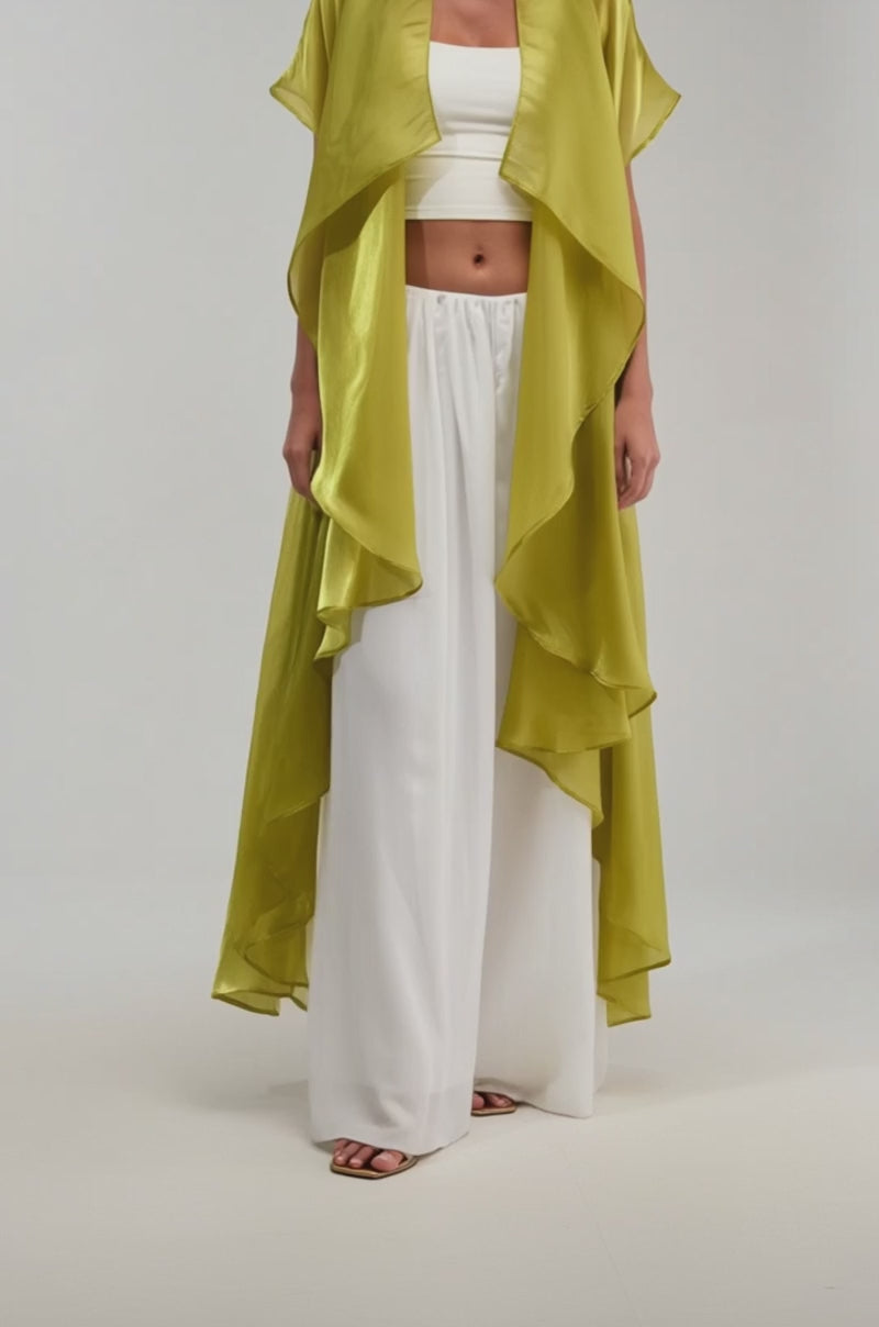 A video of a woman wearing the JULIETTE CHIFFON BLOUSE, a sheer, flowing chartreuse duster over a white crop top and wide-leg pants.