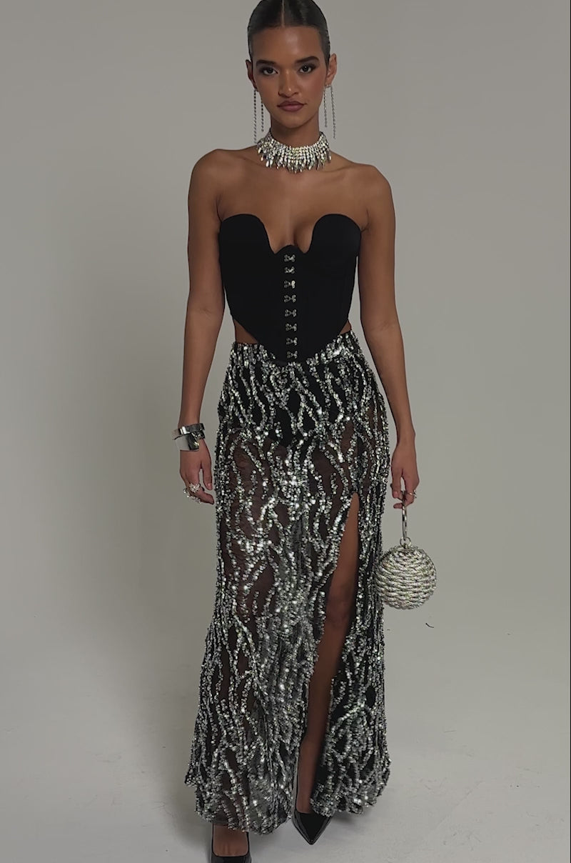 Video of woman modeling the BEAUTIFUL SEQUIN MAXI SKIRT, black pointed heels, sparkling jewelry, and holding a beaded round handbag.