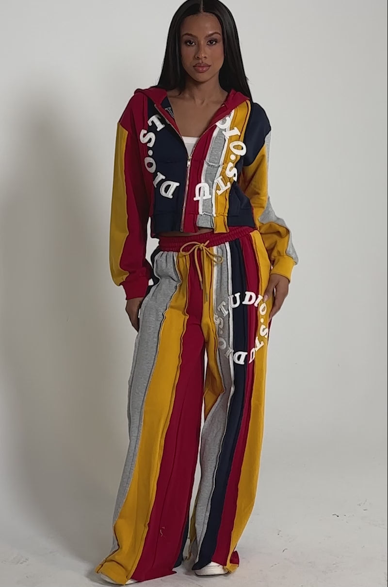 A video of a woman wearing the STUDIO LIVING JOGGER set, featuring bold printed letters and red, yellow, gray, and navy stripes. 