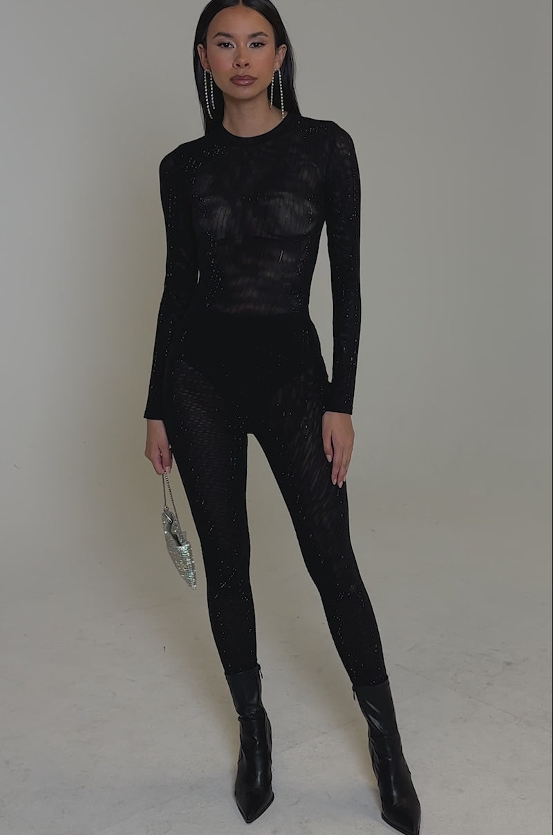 Video of woman modeling the TWINKLING LIGHTS RHINESTONE LONG SLEEVE MESH BODYSUIT IN BLACK, styled with matching pants and dangling earrings