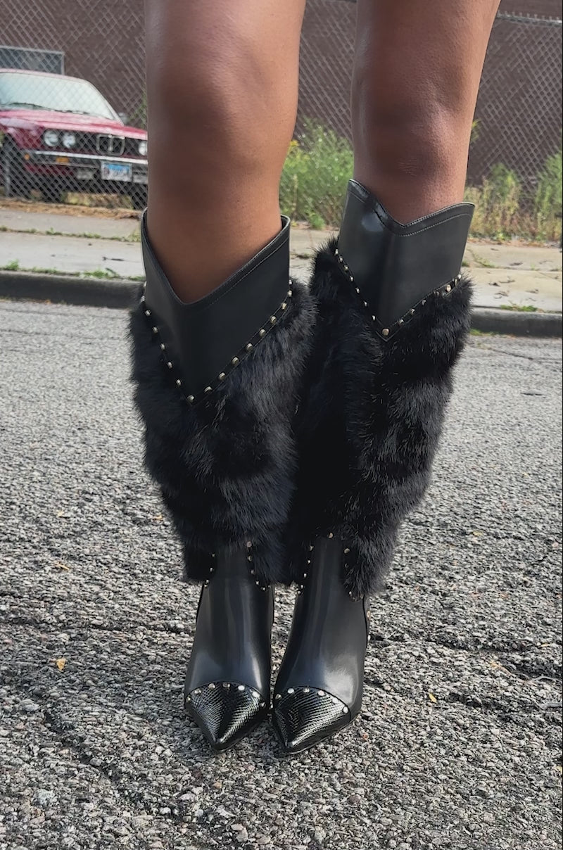 A video of a person standing outdoors in a black leather outfit with gold buttons, wearing AZALEA WANG ALISETTE BLACK FUR BOOTS. 