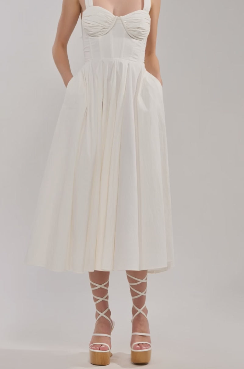 Video of woman modeling the KEEP IT LOWKEY POPLIN MIDI DRESS IN WHITE, which features a fitted corset bodice and flared skirt. She pairs it with light-colored lace-up platform heels.