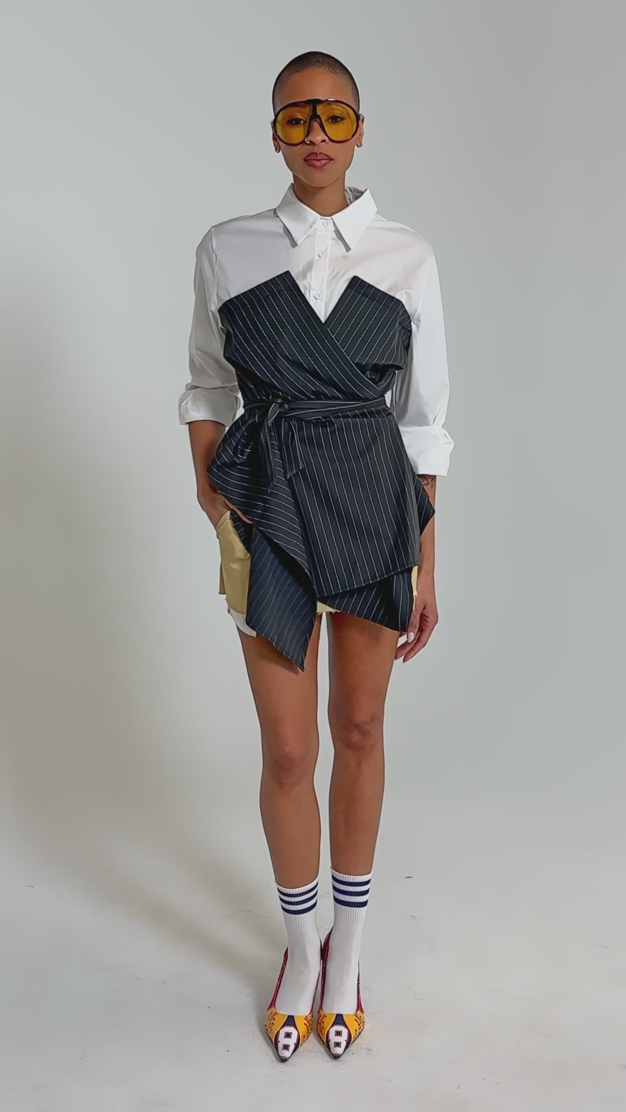 Video of woman modeling the BUSINESS ONLY BUTTON DOWN, and beige shorts, showcasing modern statement dressing against a plain background.