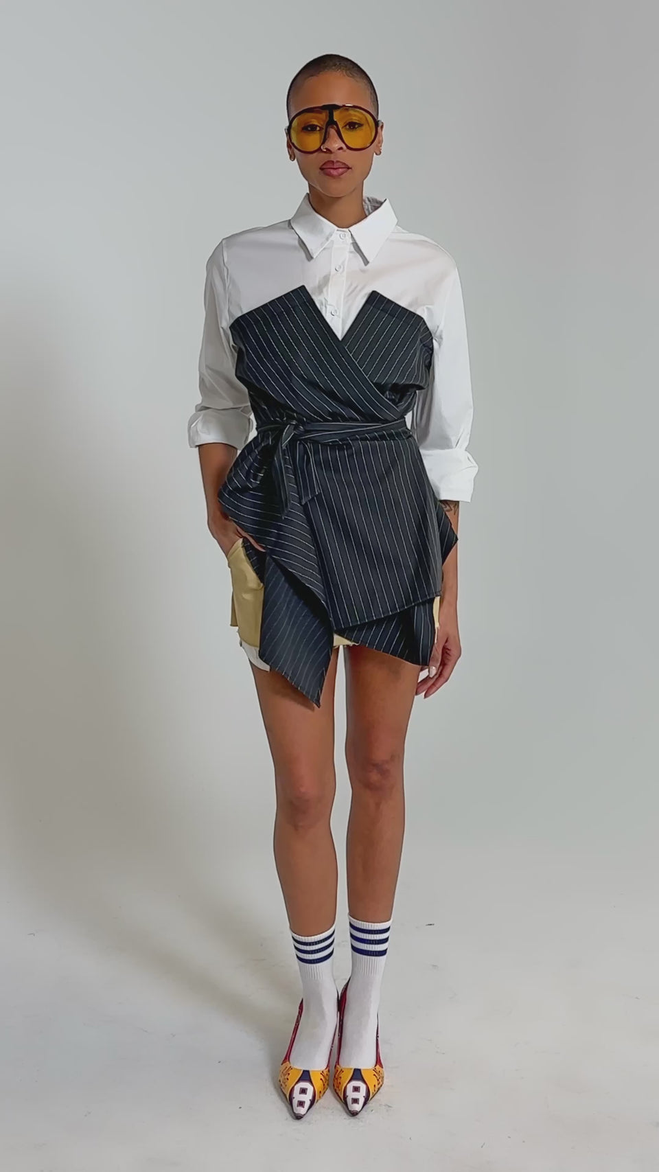 Video of woman modeling the BUSINESS ONLY BUTTON DOWN, and beige shorts, showcasing modern statement dressing against a plain background.