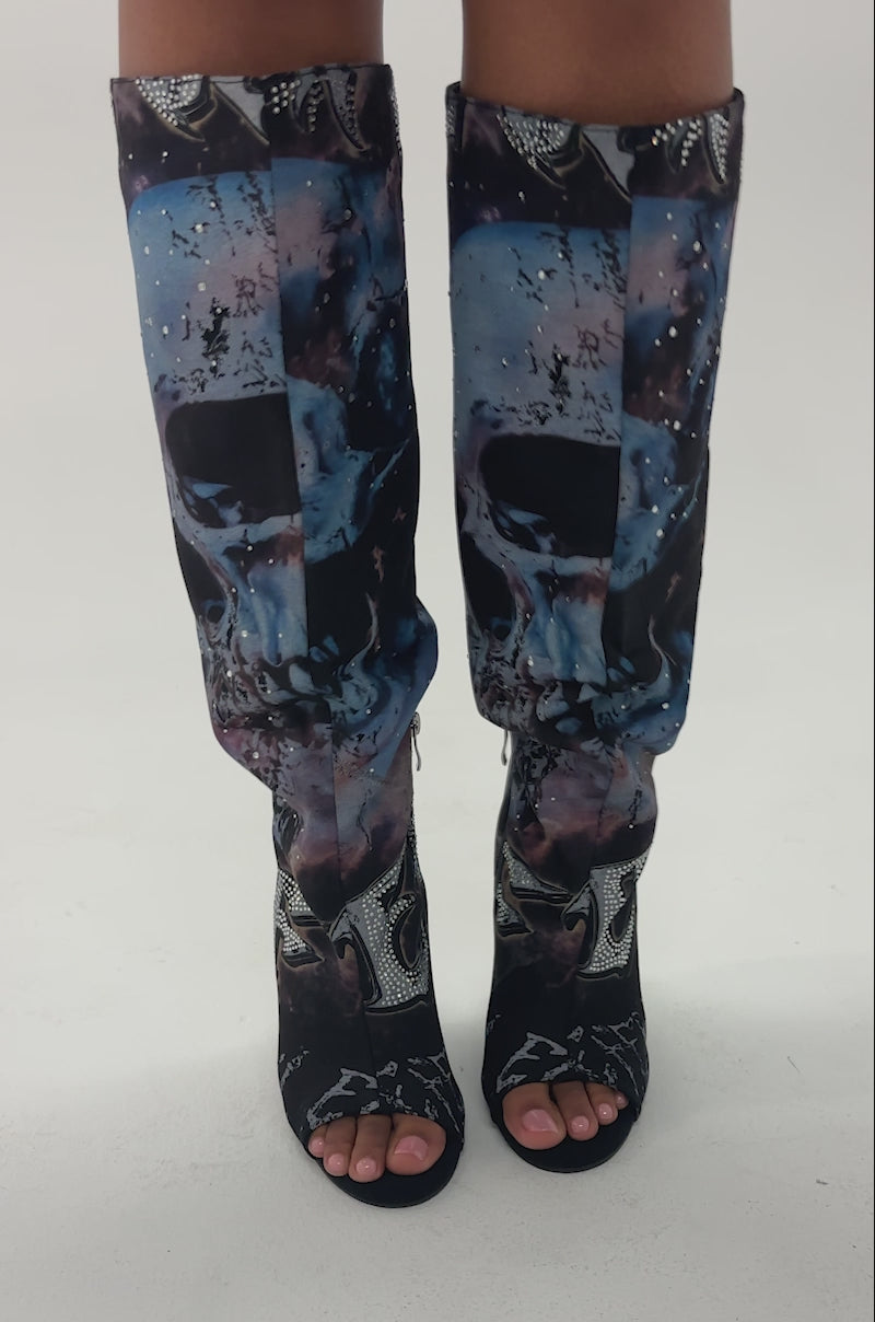 Video of woman modeling the AKIRA GOLD NINE LIVES GRAPHIC OPEN TOE WEDGE BOOT—knee-high boots with a galaxy print and silver embellished letters on white.