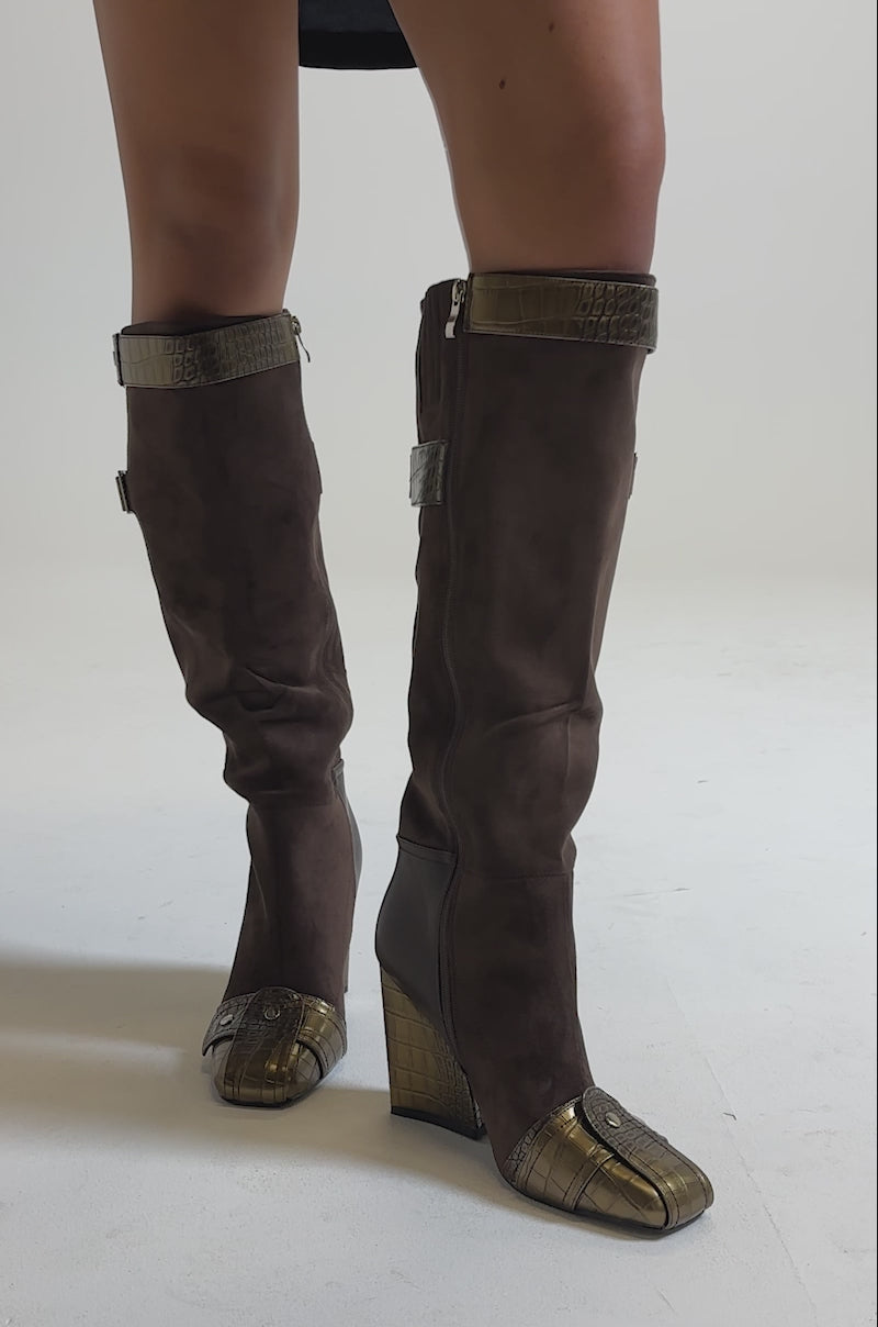 A video of a person wearing the AZALEA WANG ALLONAS BROWN KNEE HIGH CHUNKY BOOT, featuring brown suede, metallic gold accents, and wedge heels for a chic look against a neutral background.