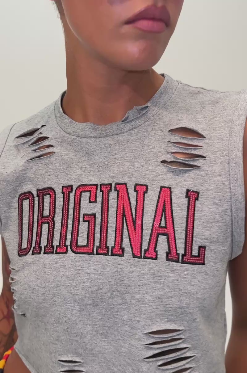 Video of a woman modeling the ORIGINAL SEQUIN CROPPED MUSCLE TEE, a grey top with distressed details and “ORIGINAL” in bold red lettering. 