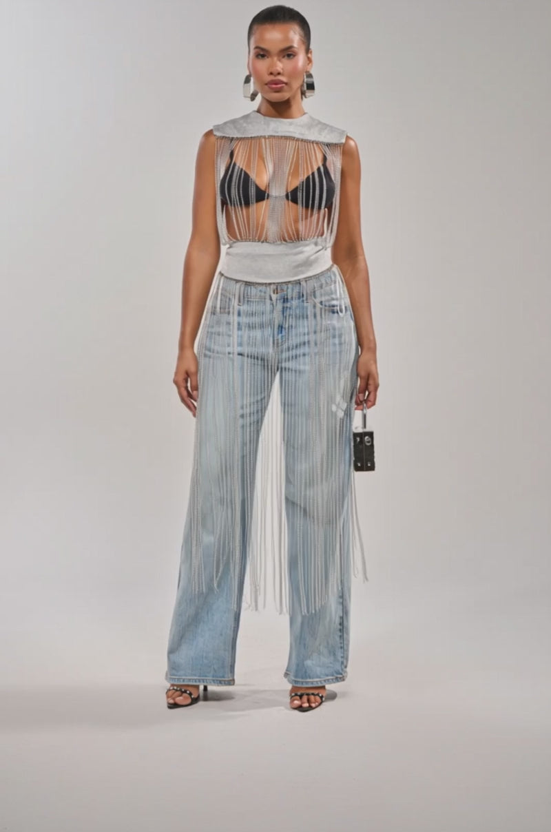 Video of woman modeling the ARK SLEEVELESS CHAIN TOP—a silver chain fringe, sleeveless statement top—paired with a black bralette, light blue high-waisted wide-leg jeans, black heeled sandals, a small black purse, and a ponytail.