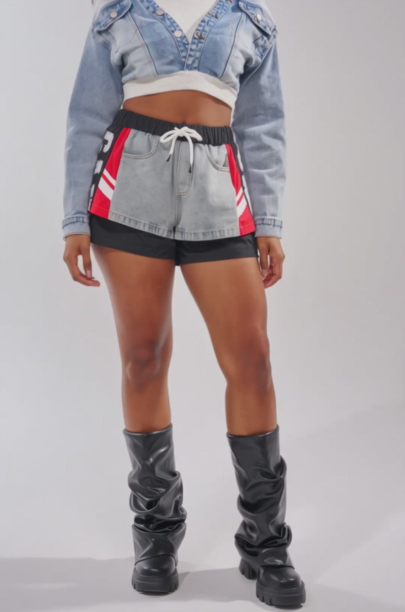 A video of a woman wearing the DOUBLE FUN SWEATSHIRT over a white top, paired with color-block athletic shorts featuring red and gray panels and black knee-high boots.