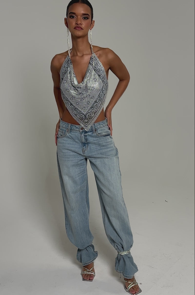 Video of woman modeling the FREESTYLE RHINESTONE COWL NECK TOP with blue jeans. Her slicked-back hair and long earrings enhance her confident pose against a plain background