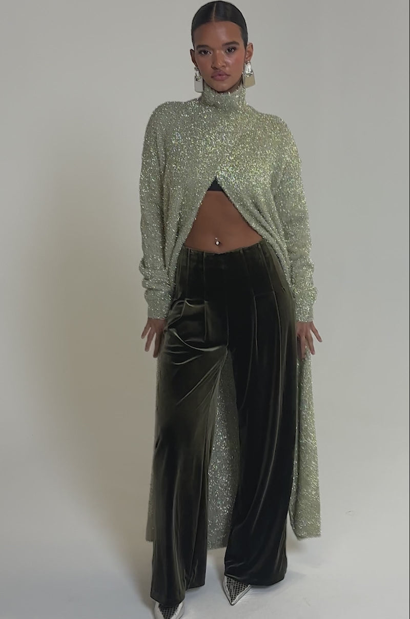 Video of woman modeling the SHOW ME IT TROUSER in high-rise, wide-leg brown velvet, paired with a sparkly long cardigan and silver pointed-toe heels. A midriff-baring look and navel piercing complete this bold, chic ensemble.