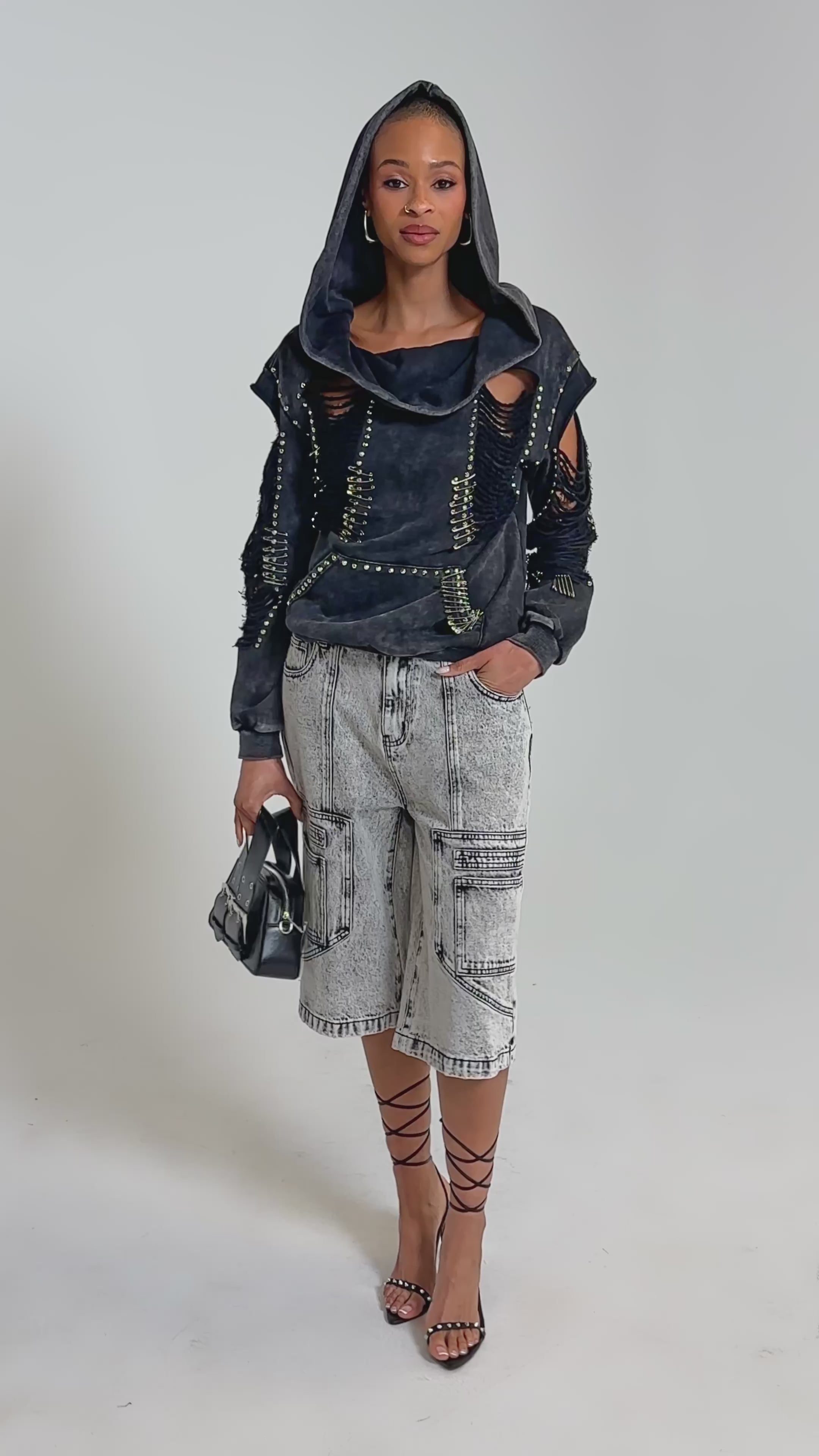 Video of woman modeling the ALL TORN UP DISTRESSED OFF THE SHOULDER SWEATSHIRT, a black top with metal studs and ripped details, styled with high-waisted, light-wash jeans featuring seam accents for an edgy streetwear look.