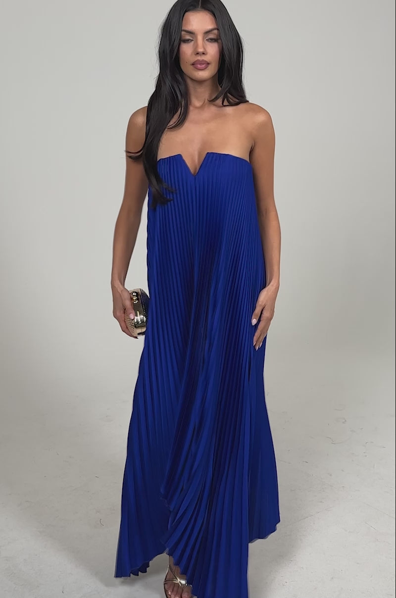 Video of woman modeling the EMERALD DREAM SLEEVELESS MAXI DRESS IN BLUE—strapless, pleated, with a sweetheart neckline—styled with a small clutch and arm cuffs, standing against a plain light background.