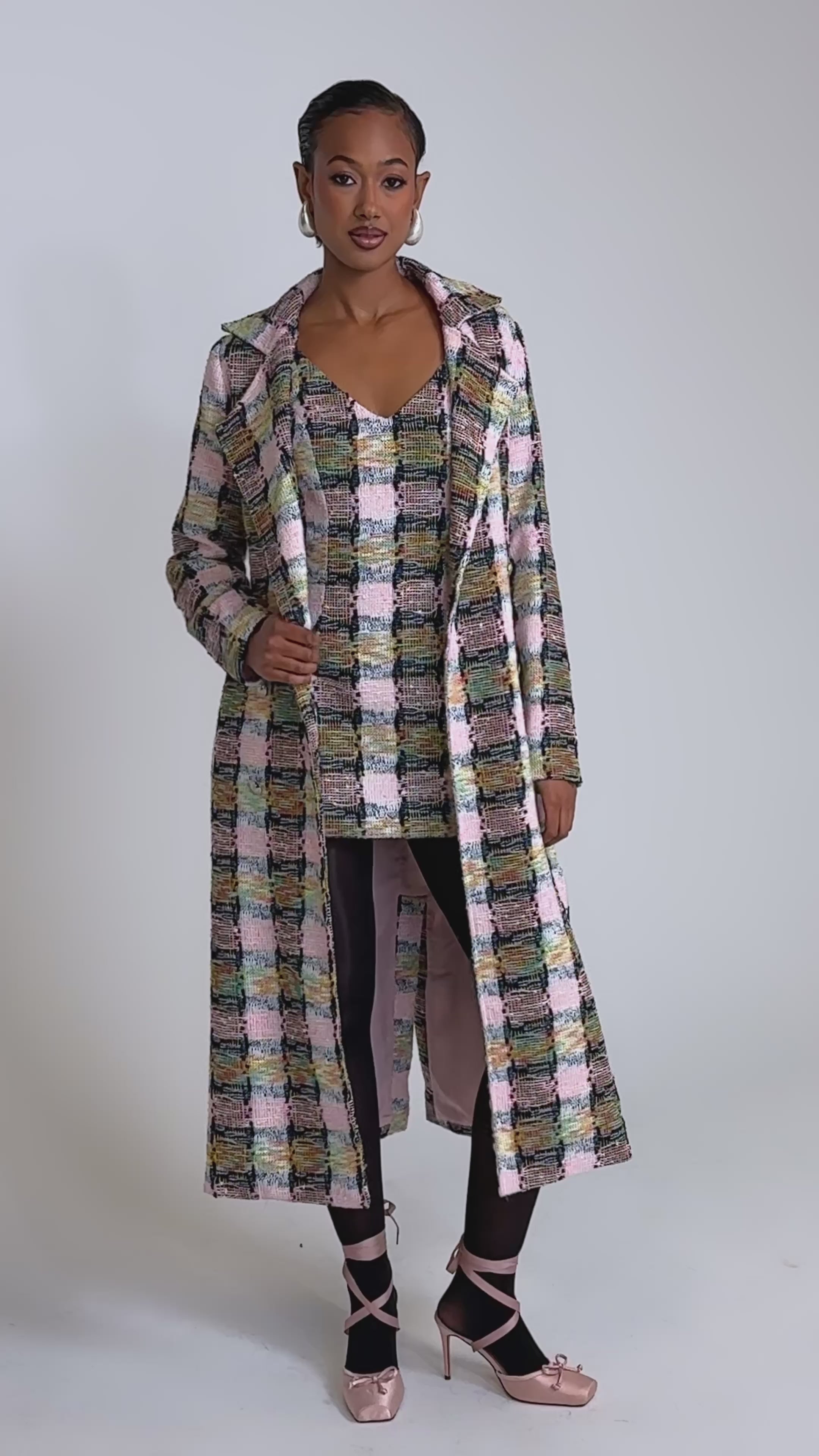 A video of a woman in the MAIN SQUEEZE TWEED MINI DRESS with a long, multicolored coat, black tights, and pink ballet flats against a plain, well-lit background.