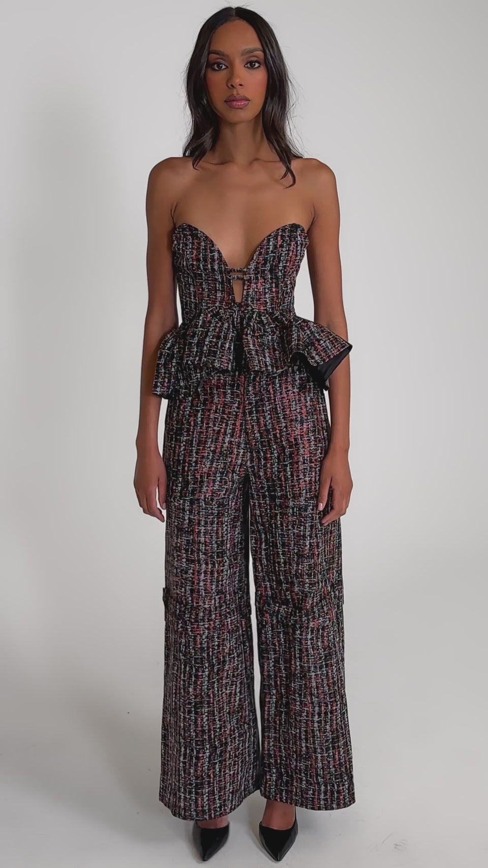 Video of woman modeling the WORK IT FAUX LEATHER PLAID CORSET in textured red and black, styled with a matching high-waisted pant, featuring a subtle sweetheart neckline. She poses against a light gray background.