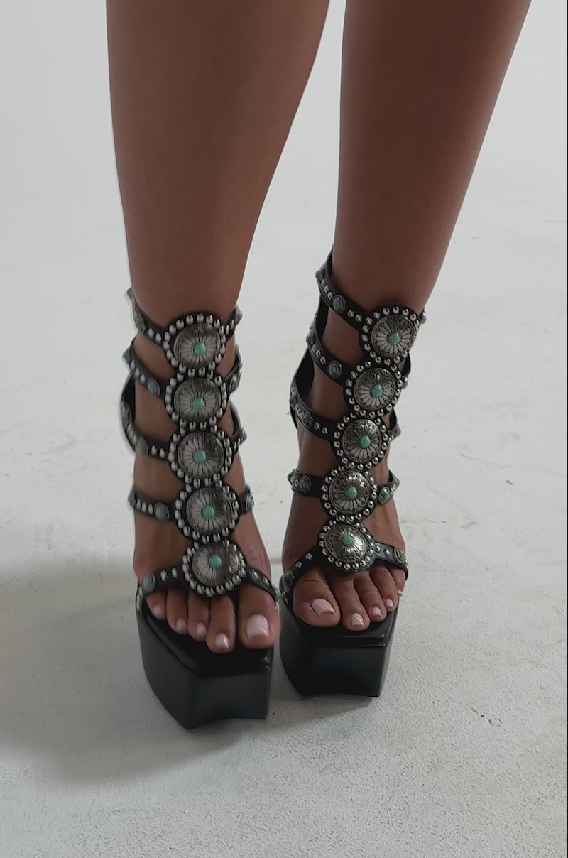 A video of a person wearing the AKIRA GOLD FUANMARA Black Embellished Sexy Stiletto PU Sandal, featuring multiple straps with jeweled accents and silver studs.