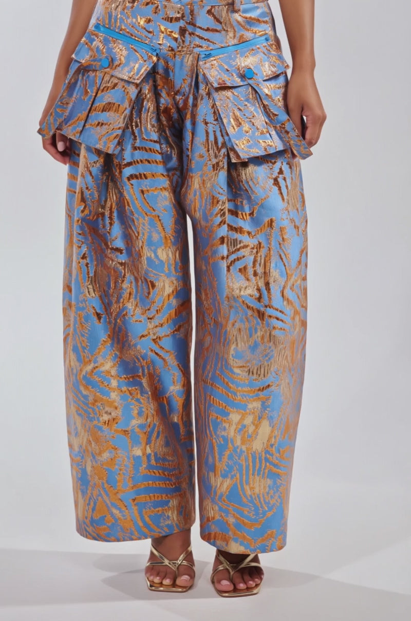 Video of woman modeling the WAYS TO GO BROCADE TROUSER, a strapless blue trouser with a high-rise waistband, gold leaf patterns, wide-leg, and ruched details. 