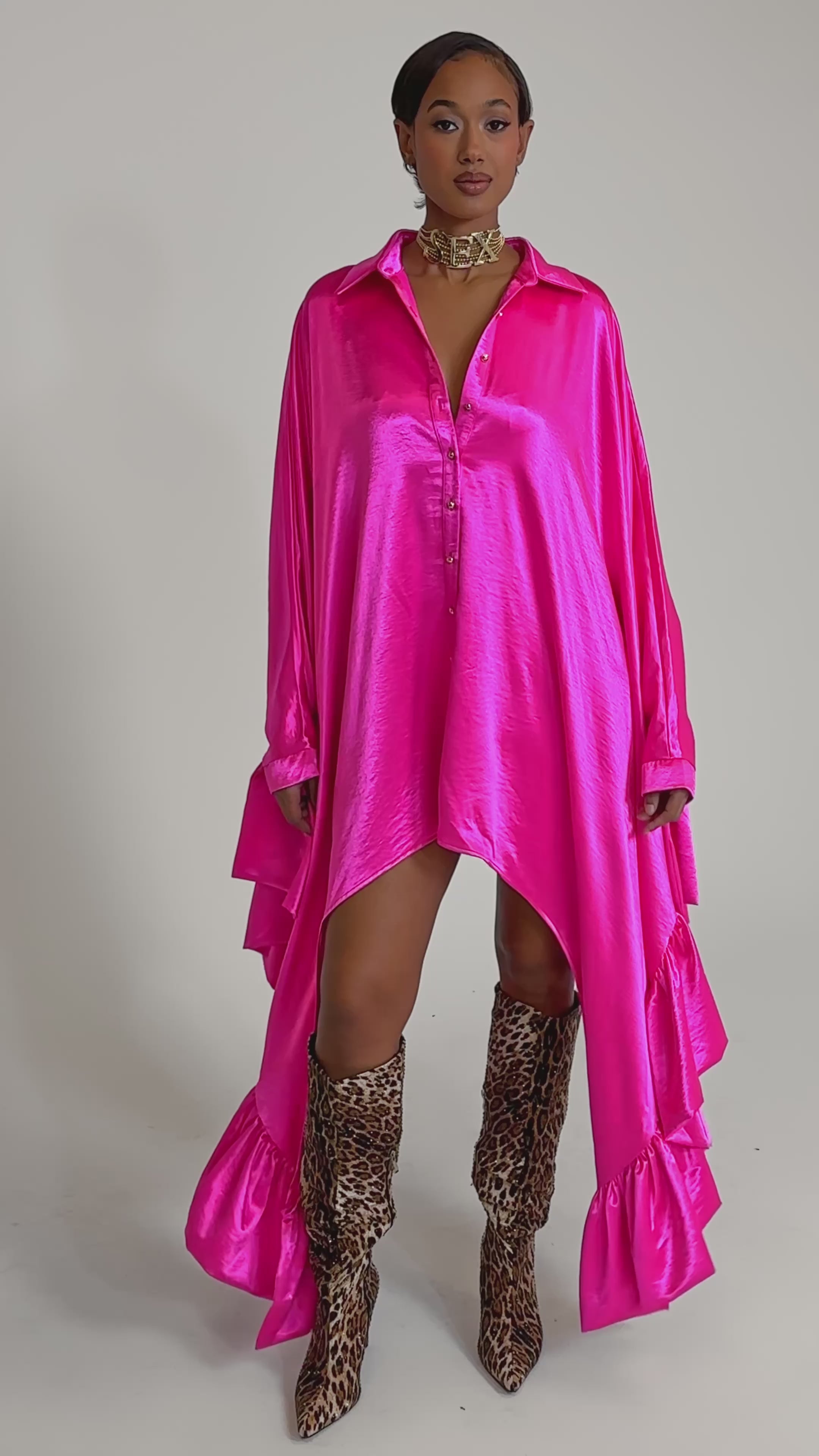 A video of a woman in the WONDERLUST Satin Long Sleeve Mini Dress in Pink, styled with leopard print knee-high boots and a gold choker for a standout look.